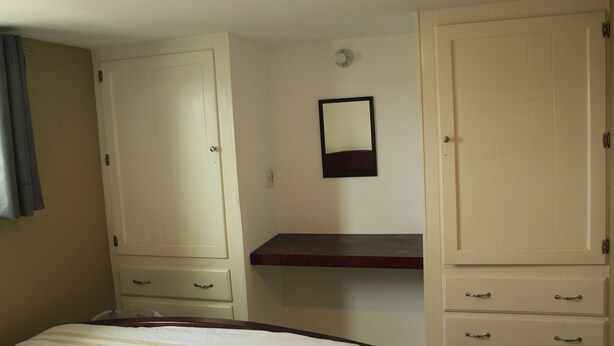 A bedroom with a bed, two wardrobes, a mirror, and a small shelf.