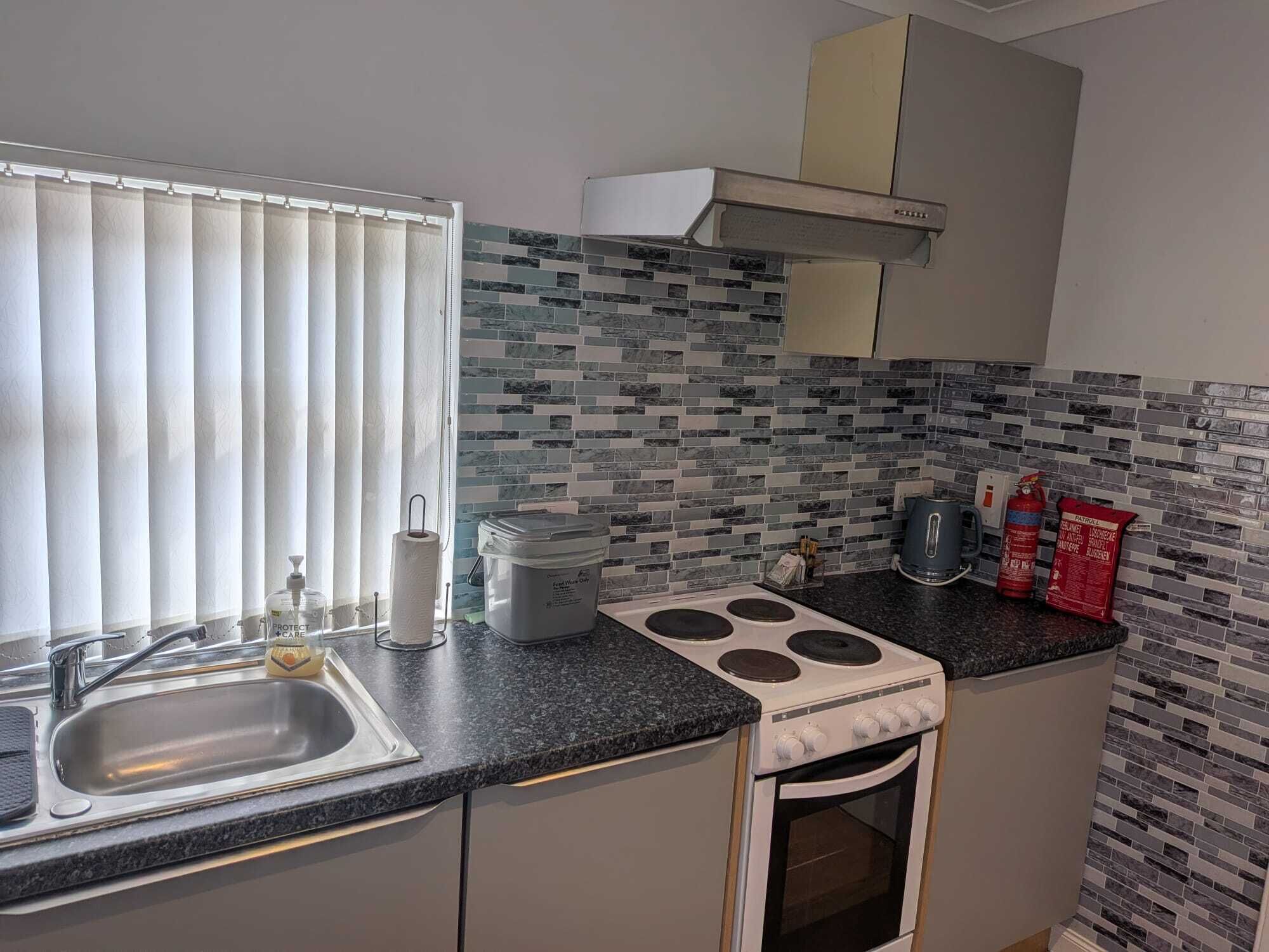 A kitchen with a sink, stove, and a window with blinds.