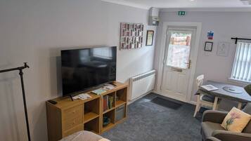 A hotel room with a television, a wooden cabinet with books, a radiator, a door with a window, and a small table with a chair.
