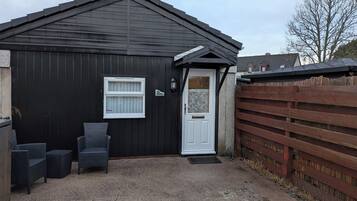 A black building with a white door and window, a wooden fence, and outdoor furniture.