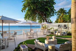 A coastal outdoor seating area with umbrellas, lounge chairs, and a view of the ocean. - Porters Place 2 | Modern West Coast Villa Near Holetown (Holetown)
