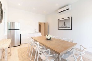 Eine moderne Küche mit einem Edelstahl-Kühlschrank, einem Esstisch mit weißen Stühlen und einem gerahmten Bild an der Wand.