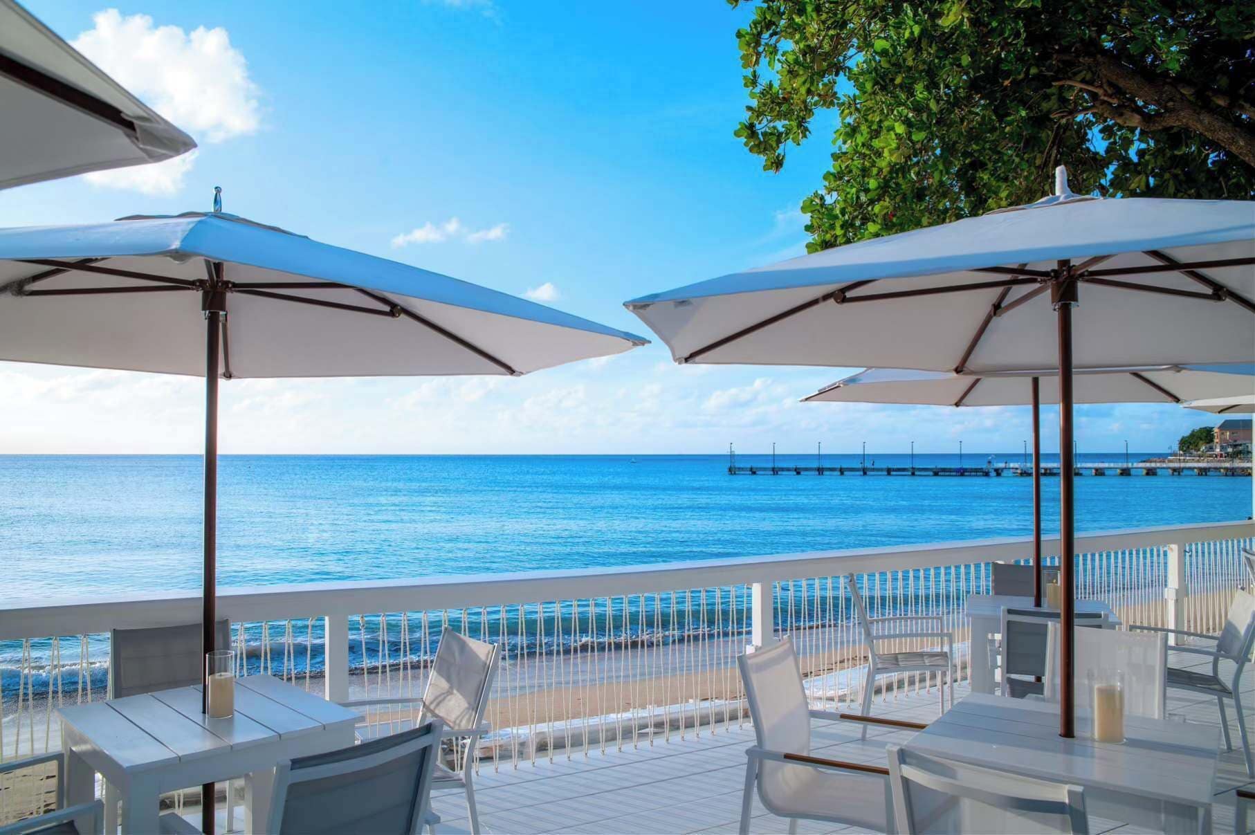 A seaside patio with white umbrellas, chairs, and a view of the ocean.