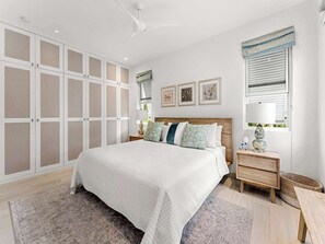 Ein Schlafzimmer mit einem großen Bett, einem Schrank mit Milchglas-Türen, einem Nachttisch mit Lampe und einem Fenster mit Jalousien.