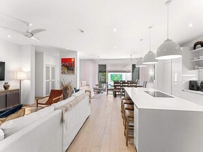 A modern kitchen with a central island, pendant lighting, and a dining area with a view to the outdoors. - Porters Place 2 | Modern West Coast Villa Near Holetown (Holetown)