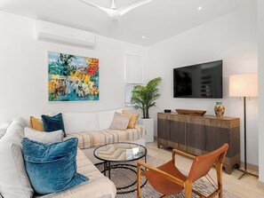 Ein modernes Wohnzimmer mit Sofa, Sessel, Couchtisch, Fernseher und Kunstwerken.