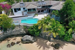 A modern house with a swimming pool, surrounded by tropical vegetation and a rocky beach. - Portobello Villa | Contemporary Beachfront Luxury on Barbados’ West Coast (St James)
