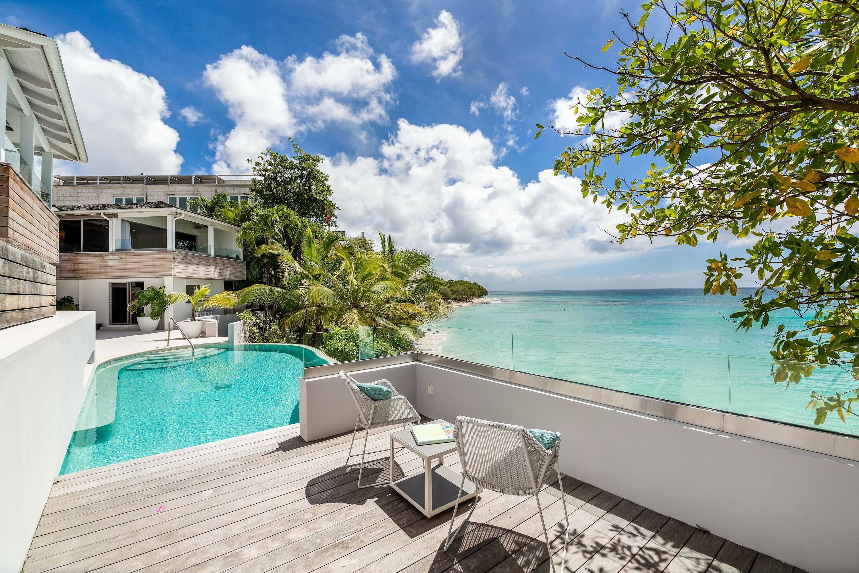 A modern house with a pool, a balcony with a view of the sea, and tropical plants.
