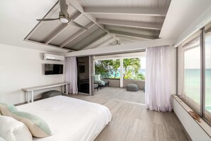 A modern bedroom with a bed, a TV, an air conditioning unit, and a view of the ocean. - Portobello Villa | Contemporary Beachfront Luxury on Barbados’ West Coast (St James)