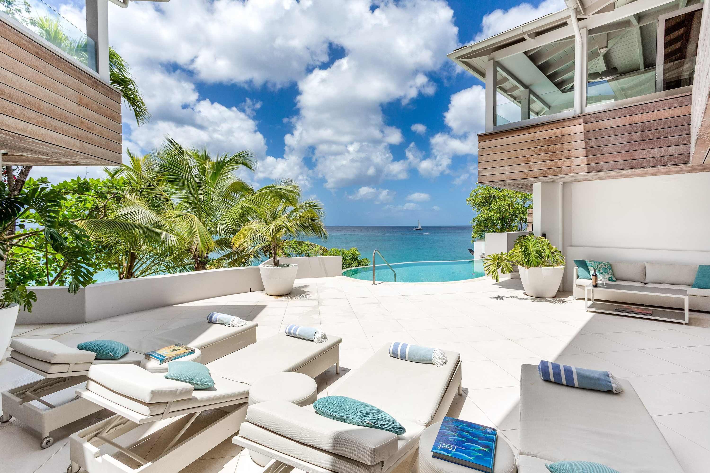 A modern outdoor lounge area with multiple sun loungers, a pool, and a view of the ocean.