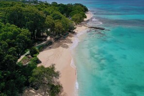 Vista aerea di una spiaggia con acque turchesi cristalline e una fitta vegetazione verde.