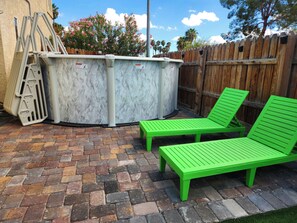 A patio area with a brick floor, two green lounge chairs, a wooden fence, and a metal structure. - Large Vacation House w/ Game Room 10-min Down Town (Las Vegas)
