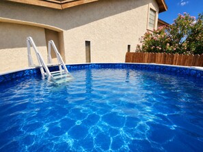Una piscina amb aigua clara i blava, una terrassa de fusta i una tanca de fusta.