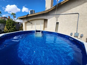 A swimming pool with a clear blue water surface, surrounded by a stone border, and a ladder leading into the water. - Large Vacation House w/ Game Room 10-min Down Town (Las Vegas)