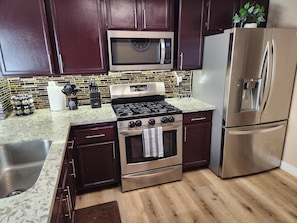 A kitchen with dark cabinets, stainless steel appliances, a microwave, stove, oven, and a refrigerator. - Large Vacation House w/ Game Room 10-min Down Town (Las Vegas)