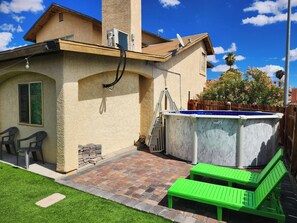 Une maison avec un jardin à l’arrière, comprenant une piscine, un patio avec un banc vert et un petit espace jardin.