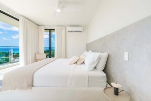 A modern bedroom with a large bed, a view of the sea, and an air conditioning unit. - Monkey Ridge | Contemporary Luxury with Panoramic Sea Views (Lower Carlton)
