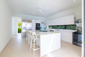A modern kitchen with white cabinetry, a central island with bar stools, and a built-in oven. - Monkey Ridge | Contemporary Luxury with Panoramic Sea Views (Lower Carlton)