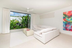 A modern living room with a white sofa, a coffee table, and a large window with curtains. - Monkey Ridge | Contemporary Luxury with Panoramic Sea Views (Lower Carlton)