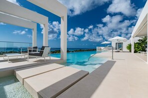 A modern outdoor pool area with clear blue water, white lounge chairs, and a view of the ocean. - Monkey Ridge | Contemporary Luxury with Panoramic Sea Views (Lower Carlton)