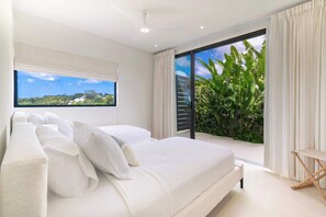 Ein Schlafzimmer mit einem großen Bett, einem Fenster mit Aussicht und einer Glastür zu einem Balkon mit Pflanzen.