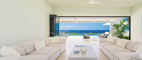 A modern living room with a large window overlooking a pool and ocean view.