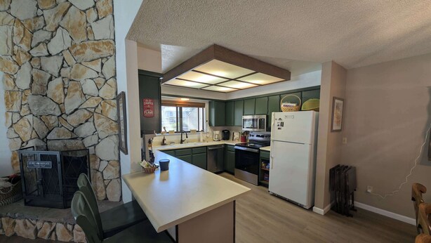 A kitchen with a stone wall, a dining area with a chair, and a refrigerator. - Paw's For Awhile - 55 Ponderosa (Plumas Eureka)
