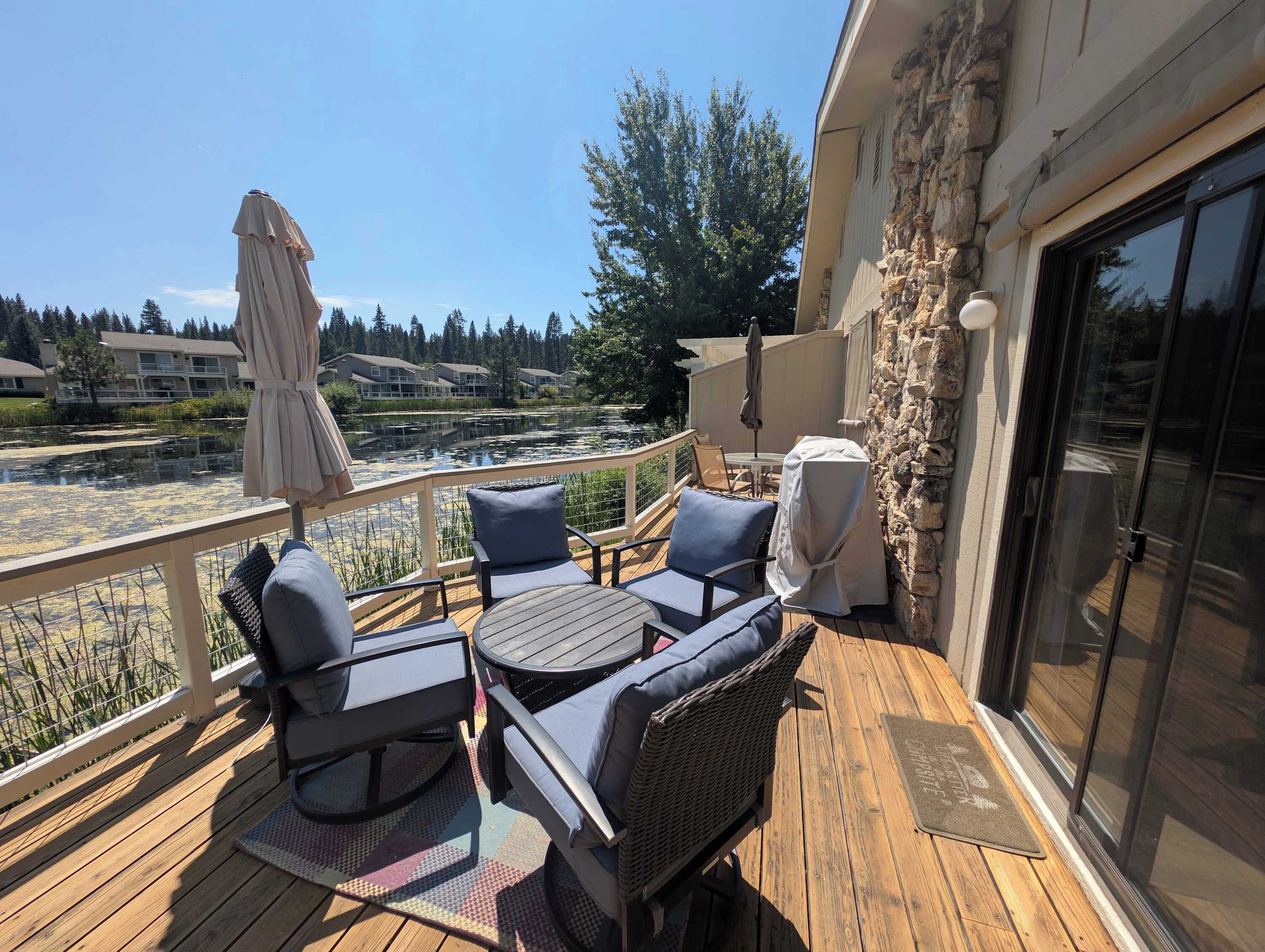 A wooden deck with outdoor furniture, a stone wall, and a view of a lake and buildings.