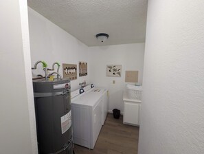 A laundry room with a water heater, washing machine, dryer, and a wall-mounted security camera. - Paw's For Awhile - 55 Ponderosa (Plumas Eureka)