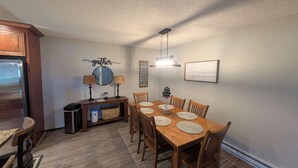 A dining area with a wooden table, chairs, a chandelier, and a wall-mounted mirror. - Pondy - 101 Ponderosa (Plumas Eureka)