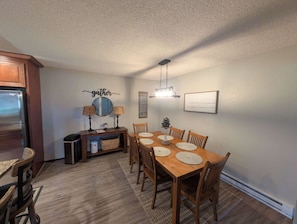 A dining area with a wooden table, chairs, a chandelier, and a wall-mounted mirror. - Pondy - 101 Ponderosa (Plumas Eureka)
