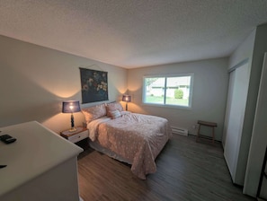 A bedroom with a bed, two bedside lamps, a nightstand, a small table, and a window with blinds. - Pondy - 101 Ponderosa (Plumas Eureka)
