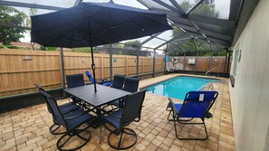 Eine Terrass mit Pool, Tisch und Stühlen sowie einem überdachten Sitzbereich.