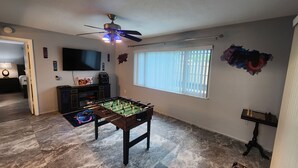 A room with a foosball table, a ceiling fan, a television, and a window with blinds. - 3-bedroom house in peaceful Port Richey with AC comfort (Port Richey)