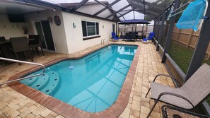 Una piscina interior con solárium de baldosas, un patio cubierto y mobiliario exterior.