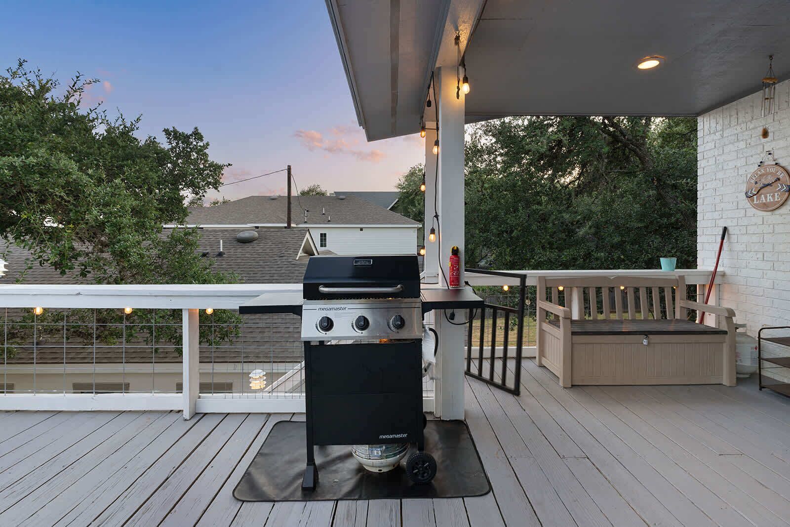 A barbecue grill on a wooden deck with a railing, a wall clock, and a bench.