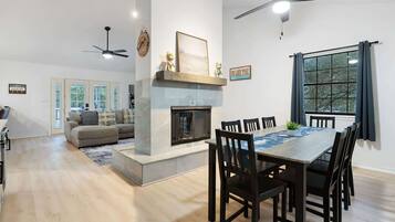 A modern living room with a fireplace, dining area with a table and chairs, and a ceiling fan.