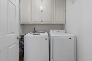 A laundry room with two white washers and dryers, a door, and white cabinets above.