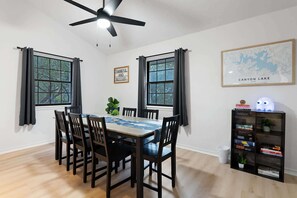 A dining area with a table, chairs, a ceiling fan, and a bookshelf.