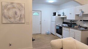 Cocina compacta con armarios blancos, un refrigerador, estufa y microondas. Se aprecia un cuadro en la pared y una puerta con un vitral.