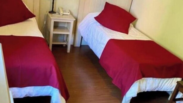 A room with two single beds, each with a red bedspread and matching pillows. There is a nightstand with a lamp and a telephone between the beds.