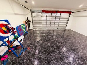 A garage with a speckled floor, a red garage door, and various colorful toys and equipment on the left. - Waterfront Oasis: A peaceful escape in Cape Coral (Cape Coral)