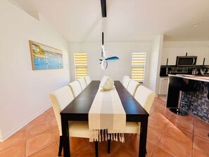 A dining area with a black table, beige chairs, and a white table runner. There is a painting on the wall and a kitchen area with a microwave and stove. - Waterfront Oasis: A peaceful escape in Cape Coral (Cape Coral)