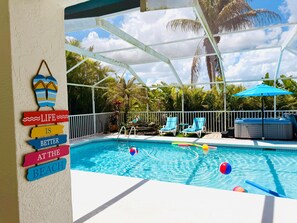 Un espace piscine équipé de chaises longues, d’un jacuzzi et d’un panneau affichant la phrase suivante : « La vie est plus belle à la plage. »
