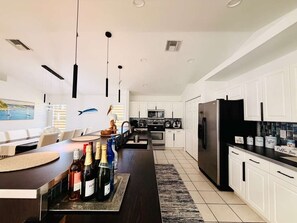 Une cuisine moderne avec des meubles blancs, un îlot central orné de bouteilles et un coin repas avec des chaises.