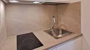 A compact kitchen with a built-in induction cooktop, a stainless steel sink, and white cabinetry. - The Two Olive Trees - North (Campo nell'Elba)