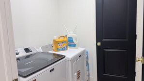 A laundry area with a washing machine, a dryer, and detergent bottles. - Luxury Living @ SLC/Airport Ski/Hike/EV Charging - 5 Bed 5 Bath (West Valley City)