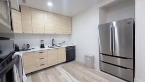 A modern kitchen with light wood cabinets, a stainless steel refrigerator, a dishwasher, and a coffee maker. - Luxury Living @ SLC/Airport Ski/Hike/EV Charging - 5 Bed 5 Bath (West Valley City)
