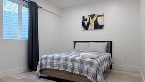 A bedroom with a bed, a window with curtains, a wall-mounted artwork, and a bedside table. - Luxury Living @ SLC/Airport Ski/Hike/EV Charging - 5 Bed 5 Bath (West Valley City)