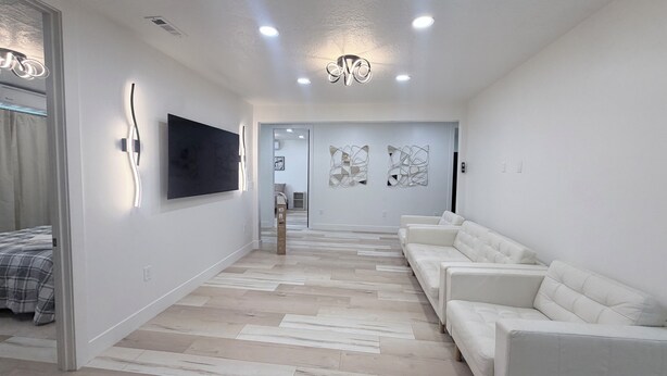 A modern living room with a white sofa, a flat-screen TV mounted on the wall, and a patterned floor. - Luxury Living @ SLC/Airport Ski/Hike/EV Charging - 5 Bed 5 Bath (West Valley City)